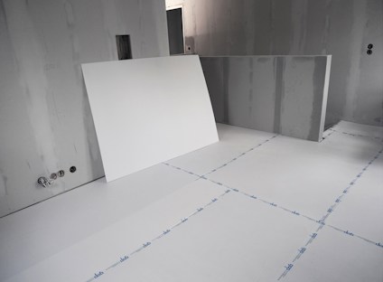 Rum under renovering med vita gipsskivor lutade mot en vägg, oslipade väggar och omärkta golvskivor.