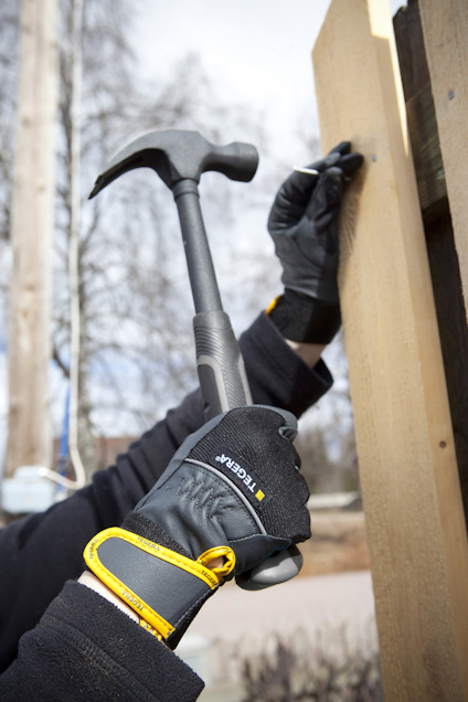 Hand håller en hammare och spikar på en träplanka. Har svarta handskar på sig.