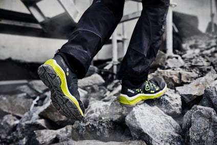 Person i svarta byxor går på stenar i svart och gul sko.