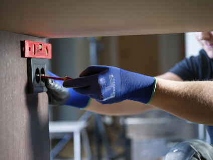 En person i blå handskar installerar eluttag i väggen med vattenpass.