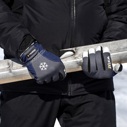 En person i svart jacka håller en trähorisontellt träbjälke med handskar märkta med "tegera" och "water".