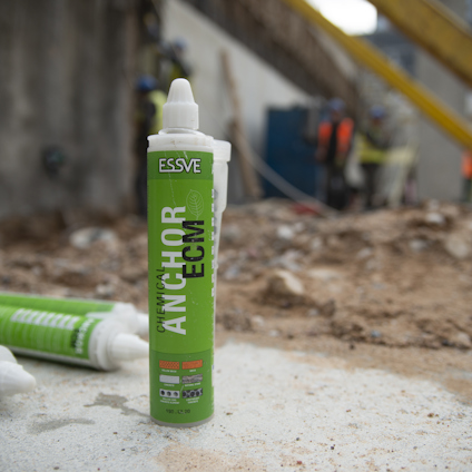 Grön tub märkt "ESSVE Chemical Anchor ECM 300". Arbetsplats i bakgrunden.