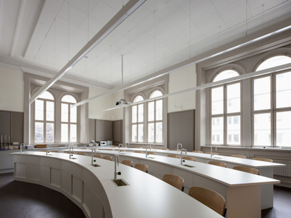 Ett modernt klassrum med bågformade fönster, ljusa väggar, trästolar och vita bord i rader.