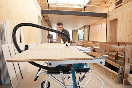 Person använder såg för att skära träskiva i ett byggprojekt inomhus.