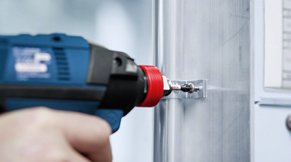 Hand using a blue and black power drill with a red drill bit on a metal surface.