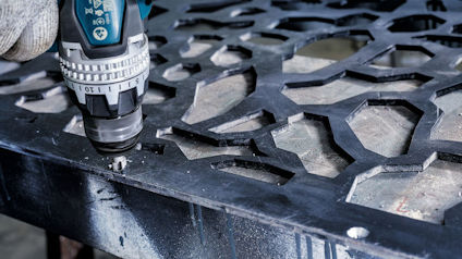 Borrmaskin borrar i ett metallgaller med hexagonala former.