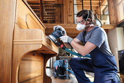 Person slipar en trämöbel med skyddsglasögon och ansiktsmask.