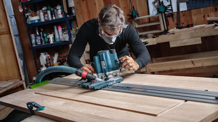 Person med sticksåg bearbetar träskiva i verkstad.