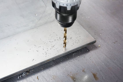 Metallbit som borras med en elektrisk borr, metallspån synliga på ytan.