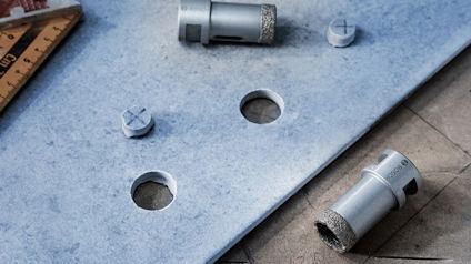 Borrade hål i ljusgrått material, omgiven av borrverktyg och en mätvinkel.