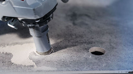 Diamantborr borrar ett hål i en grå betongplatta, omgiven av stenmjöl.