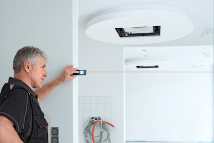 En man använder en lasermätare i ett rum med vitmålade väggar och en rund takinstallation.