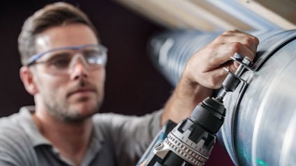En man borrar i ett metallrör och bär skyddsglasögon.