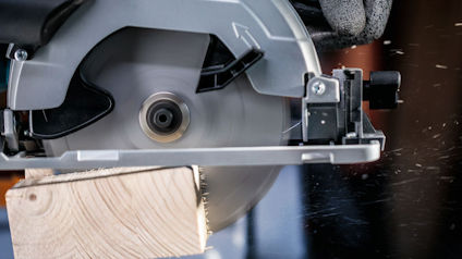 Cirkelsåg som skär genom träbit, sågspån flyger omkring.