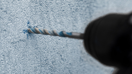 Borrmaskin borrar i en blå vägg med ett spiralborrbett.