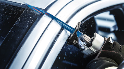 En person i skyddshandske använder en elektrisk såg för att skära genom glas och metall.