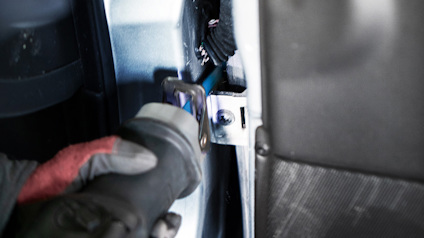 Hand i handske använder verktyg för att arbeta på metallkomponenter i en tät utrymme.