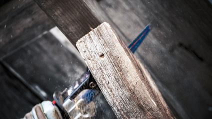 En person sågar genom en träplanka med en rund såg, träflisor flyger i luften.