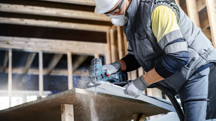 Person i skyddsutrustning som sågar plywood med en cirkelsåg i en pågående byggnadskonstruktion.