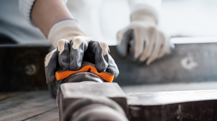 Händer med skyddshandskar arbetar med verktyg på en träyta.