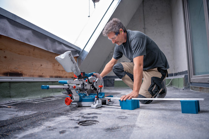 Man använder en kap- och geringssåg på en byggarbetsplats, med säkerhetsglasögon och skyddskläder.
