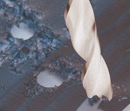 Borr i träbit med sågspån runt borrade hål.