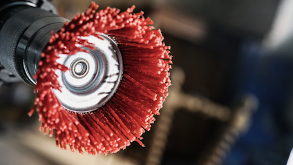 Röd roterande borste med borst i plast och metallcentrum, monterad på en elektrisk borrmaskin.