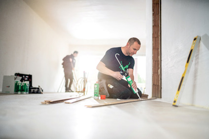 Person knästående applicerar tätningsmedel på bräda i ett renoveringsutrymme, med andra verktyg och material i närheten.