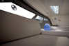 Invändig vy av en båt med dämpad belysning; sittplats, fönster, blå dryckesflaska, taklucka.